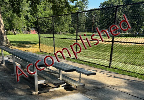 Bleachers sit next to an ADA seating pad in a park.